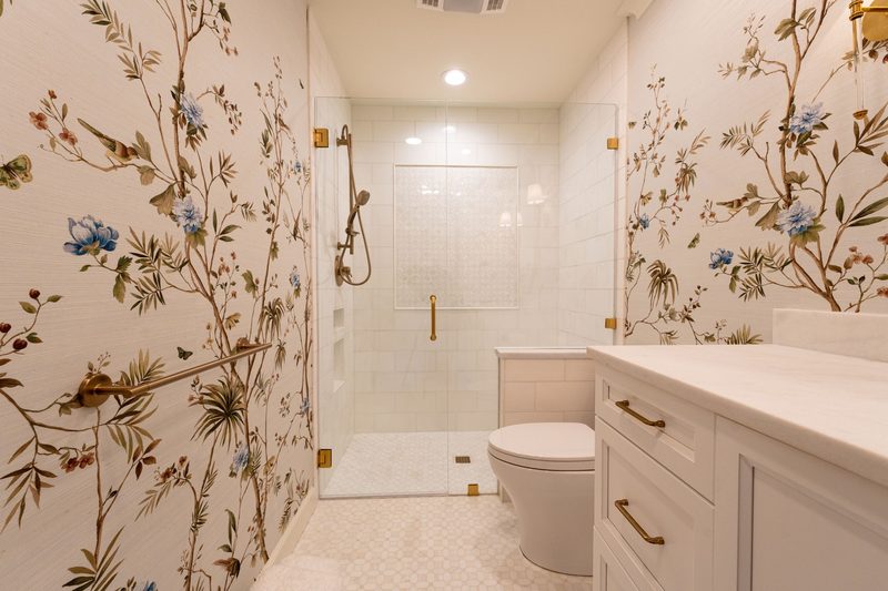 Elegant bathroom with a botanical branch-and-blossom wallpaper covering the walls beside a glass shower and marble vanity