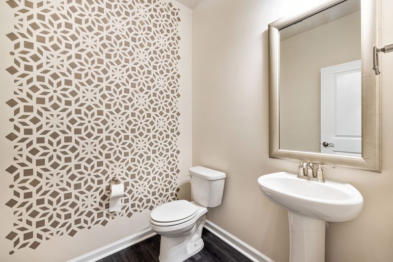 Contemporary powder room with a soft grey geometric wallpaper behind a ceramic pedestal sink and framed mirror