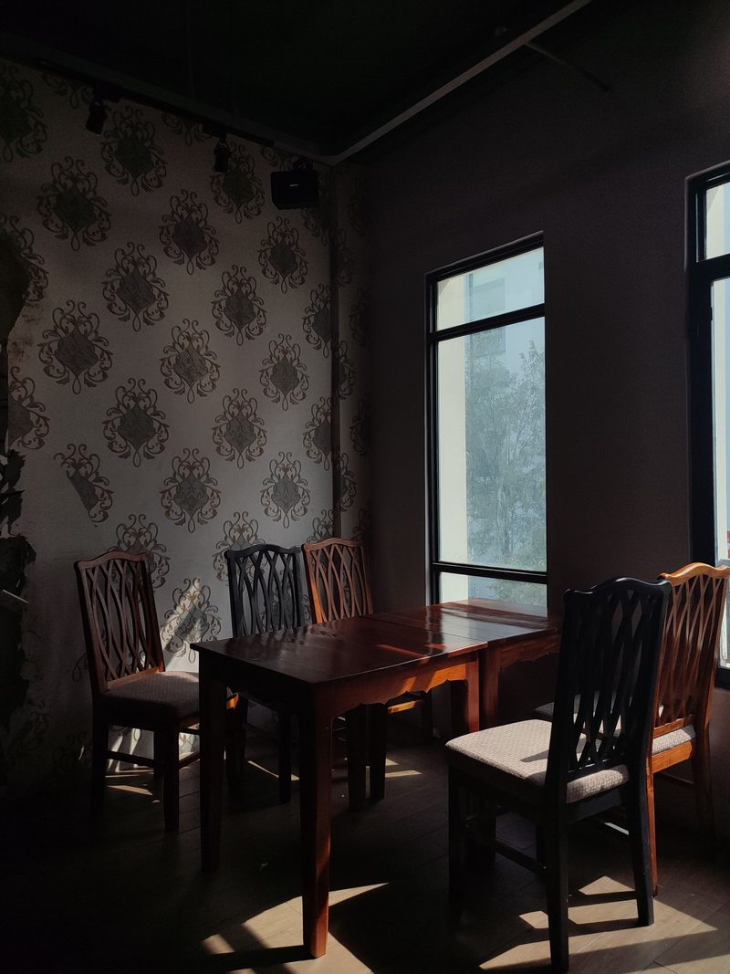 Moody dining corner with a dark damask wallpaper, wooden table and chairs, and soft light falling from a window