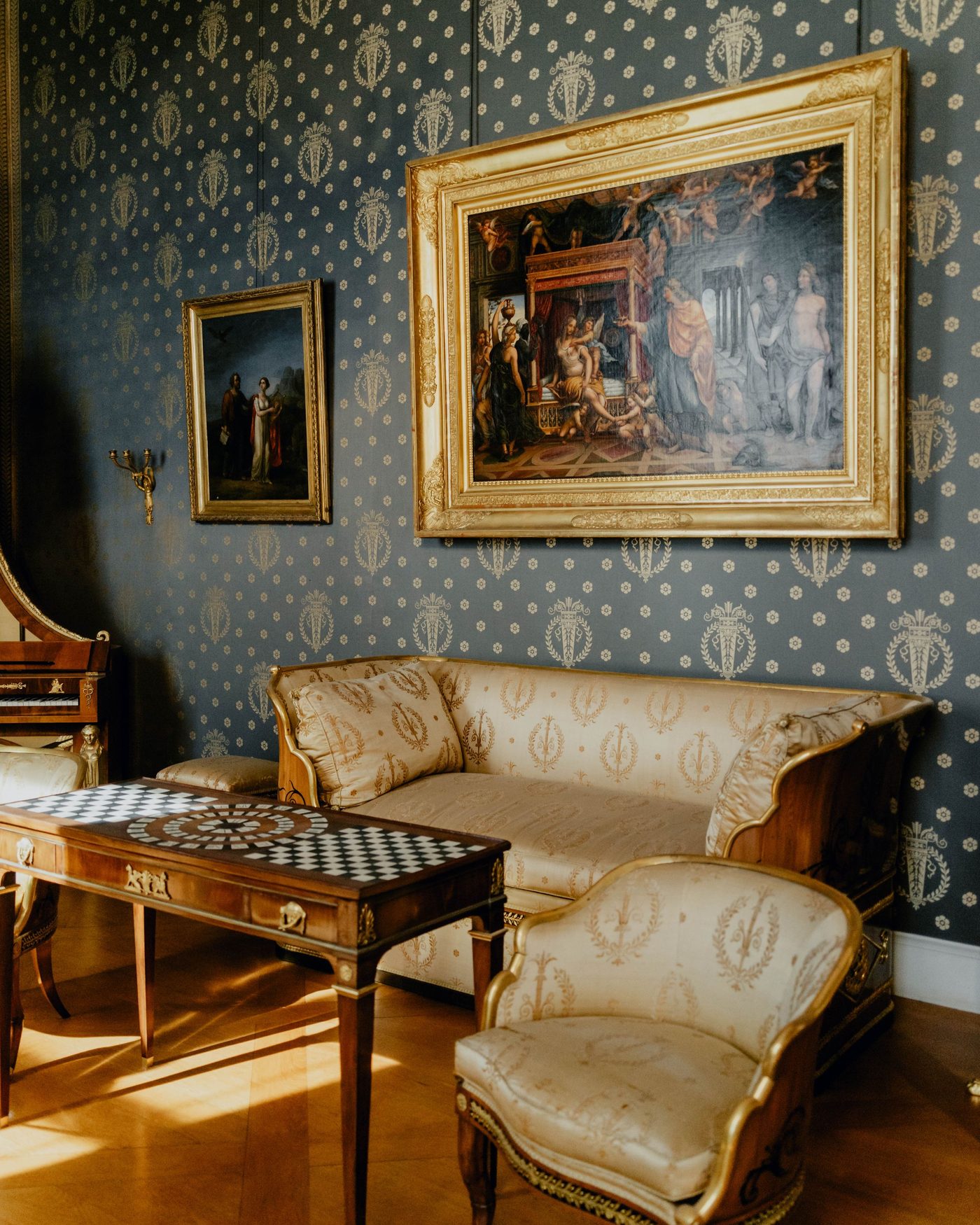 Formal sitting room with ornate blue and gold patterned wallpaper wrapping the walls, a period sofa and framed artwork