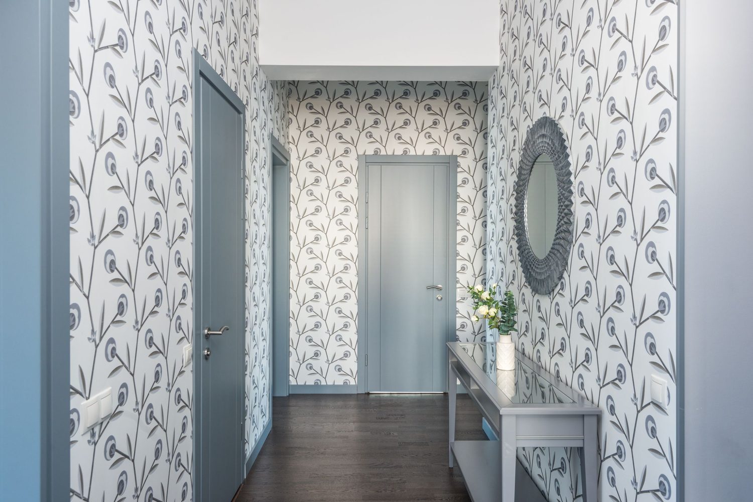 Entry hall with soft grey floral wallpaper, a console table with fresh flowers, and a decorative round mirror