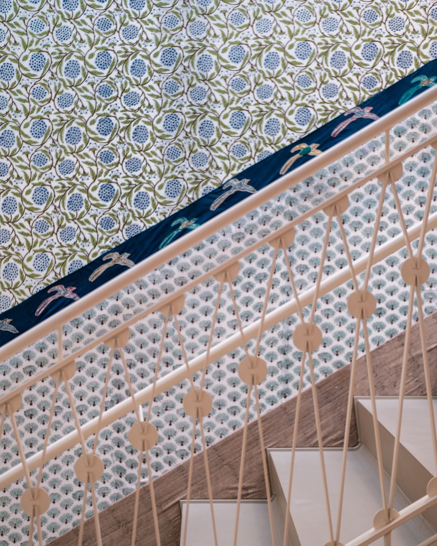 Staircase seen on a diagonal, its geometric balustrade set against a floral wallpaper running cleanly up the wall