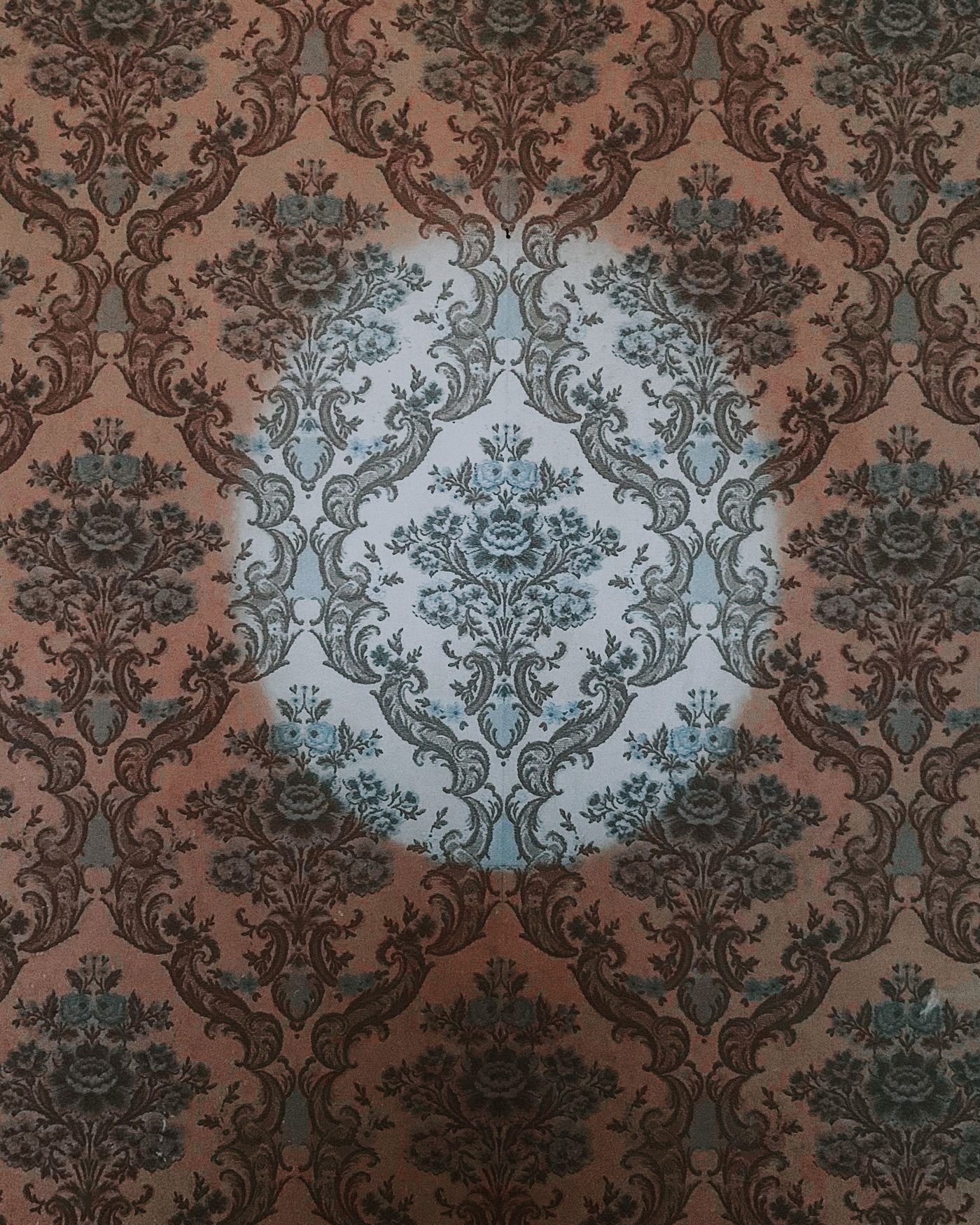 Close-up of a dark damask wallpaper showing an intricate floral medallion and the precise vertical seam between drops